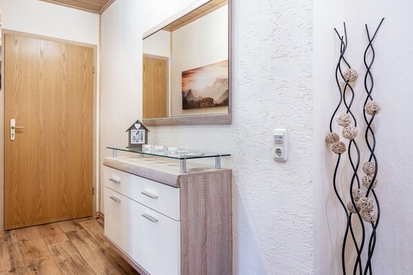 A bathroom with a wooden door, a glass sink, a mirror, and a wall-mounted decorative piece.