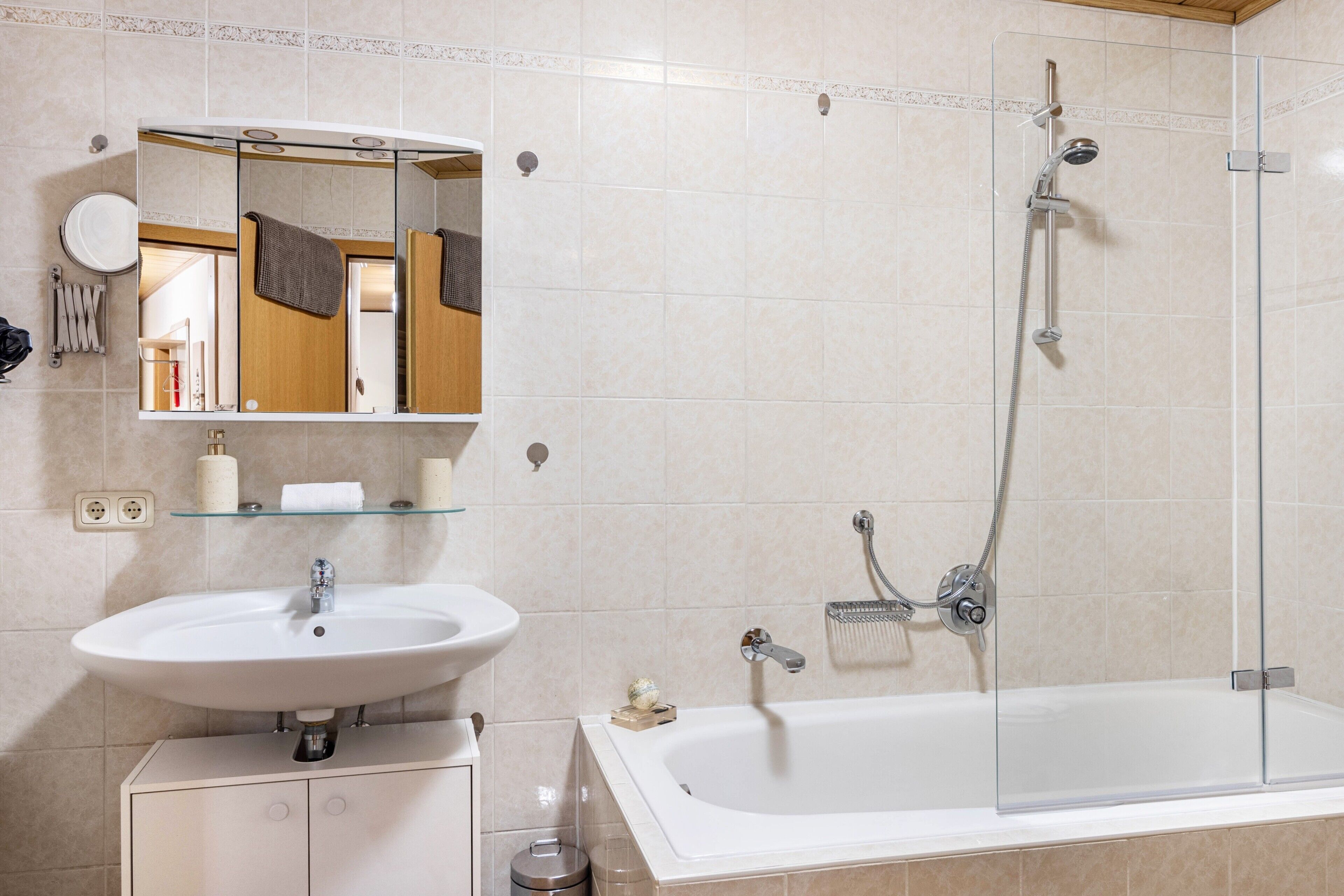 Ein Badezimmer mit Waschbecken, Spiegel, Dusche und einer in Glas abgeschlossenen Badewanne.