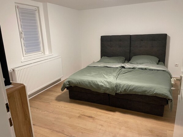 A bedroom with a bed, a window, a radiator, and a wooden floor.