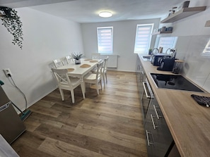 A modern kitchen with a dining area, wooden flooring, white cabinetry, and a built-in oven.