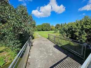 Un chemin en béton mène à une zone herbeuse, de part et d’autre de laquelle se trouvent des garde-corps en métal.
