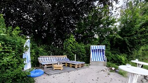 A sandy outdoor area with a wooden bench, a striped beach chair, and a small table. - Apartment 'Block' with Private Terrace, Shared Garden and Wi-Fi (Brodersby OT Schönhagen)