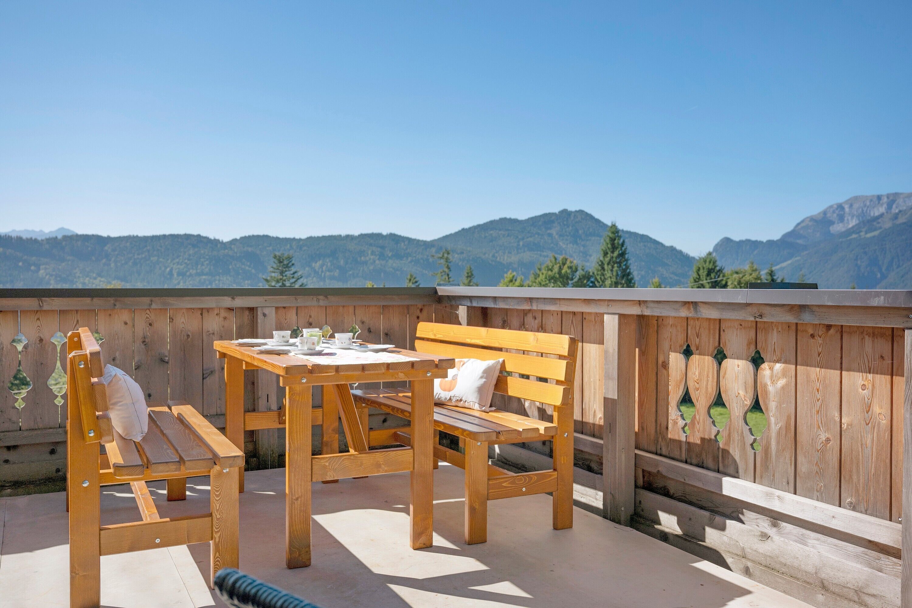 A wooden deck with a table and chairs, a wooden fence, and a mountainous backdrop.