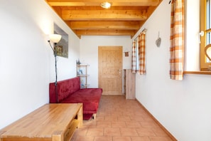 Ein gemütlicher Raum mit Holzboden, einem roten Sofa, einem Holztisch und einer Holztür.