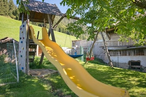 Ein Spielplatz mit Rutsche, Kletterwand und Schaukeln.