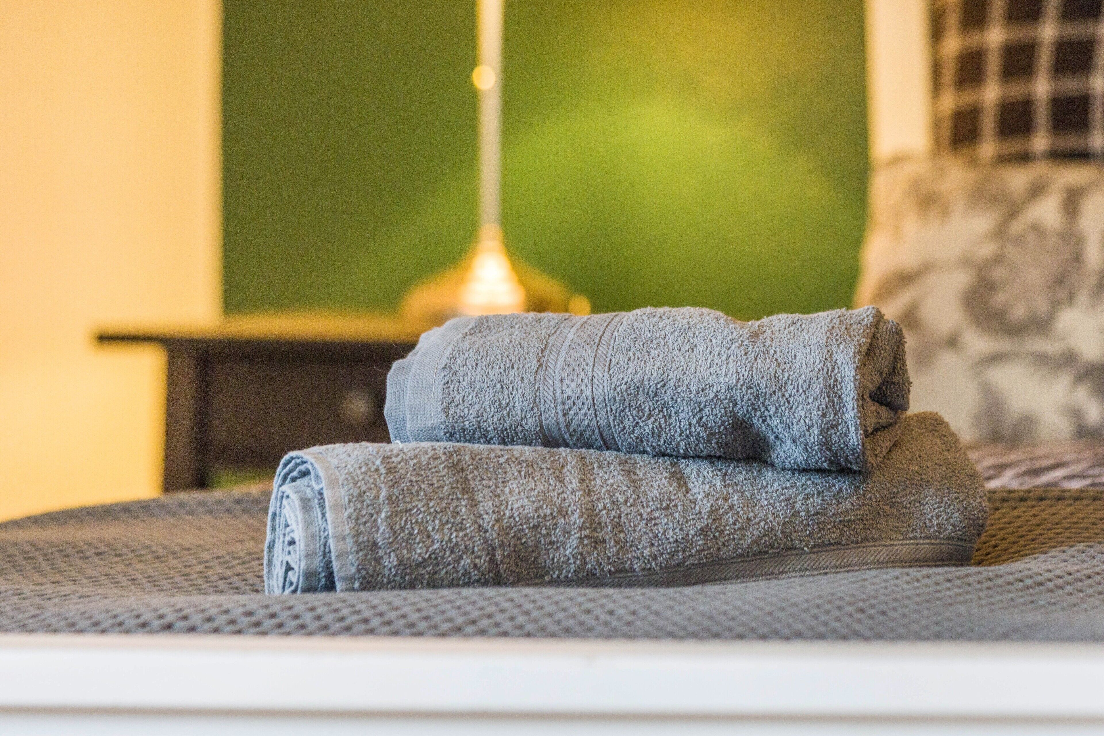 A neatly folded towel on a bed with a textured bedspread, a lamp, and a green wall in the background.