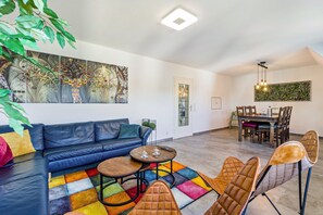A modern living room with a sectional sofa, a coffee table, and a colorful rug. There is a dining area with a table and chairs. - Apartment 'My Cocoon' with Private Terrace and Wi-Fi (Lüdenscheid)