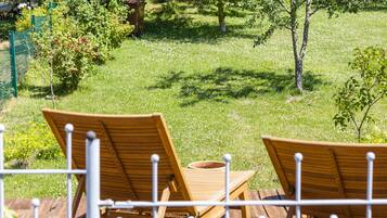 Two wooden lounge chairs on a deck with a view of a grassy yard and trees.