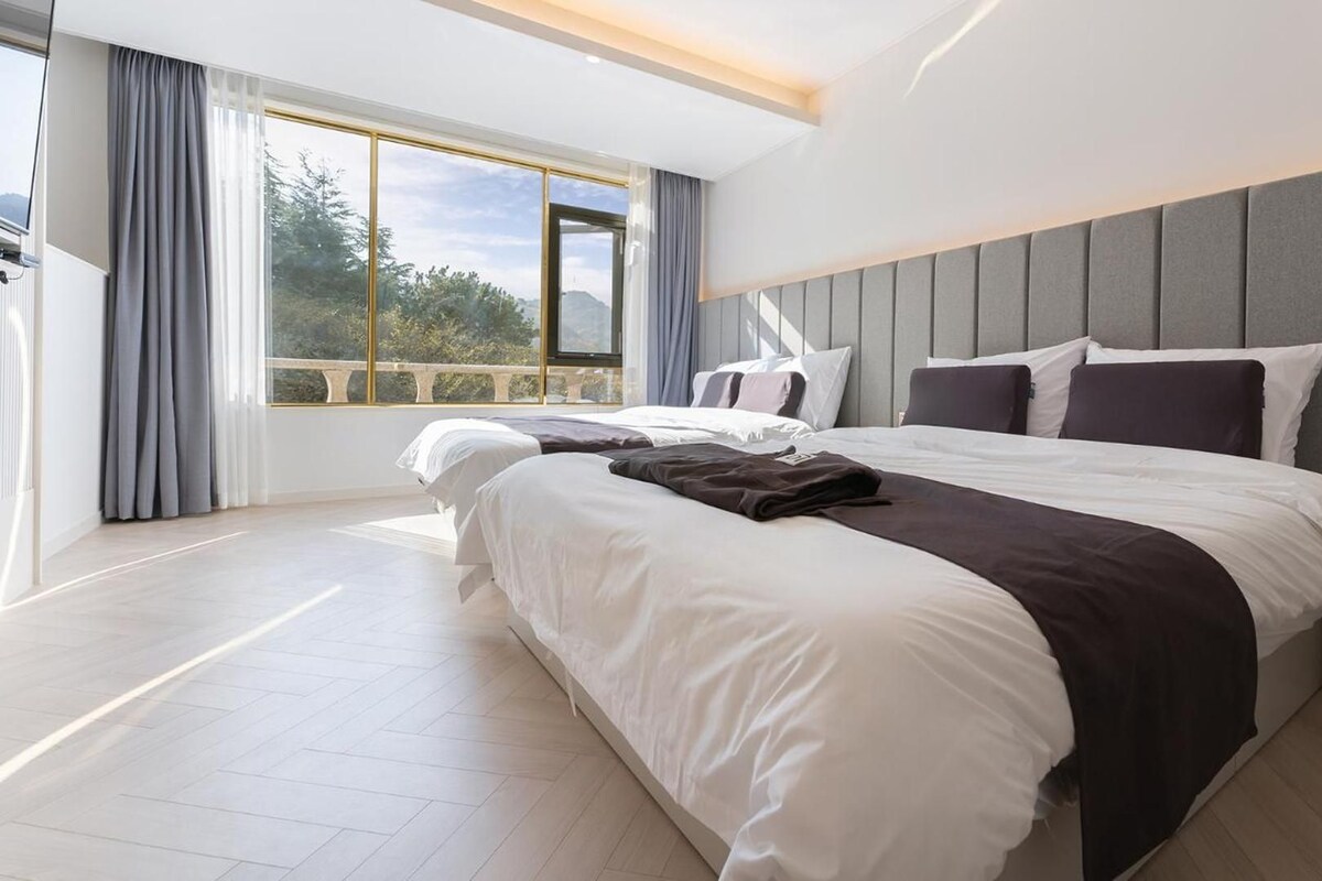 A modern hotel room with a large bed, a bedside table, and a view of the outdoors.