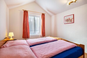 Una cama individual con ropa de cama rosa y azul, una mesita de noche con una lámpara y una ventana con cortinas.