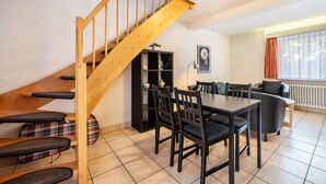 A dining area with a wooden staircase, black chairs, a table, and a black bookshelf.