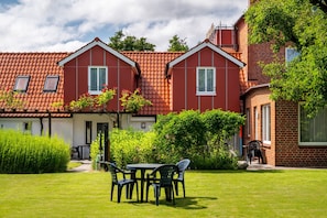 A two-story house with a red-tiled roof, a garden with a table and chairs, and a pathway leading to the entrance. - Hus achtern Diek Cuxhaven Apartment No. 2 (Cuxhaven)
