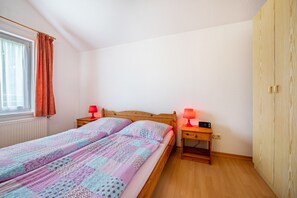 A bedroom with a wooden bed, two bedside tables with lamps, a window with curtains, and a wooden wardrobe. - Hus achtern Diek Cuxhaven Apartment No. 2 (Cuxhaven)