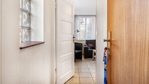 Un pasillo con una puerta blanca, un ventanal con persianas, un sillón de cuero negro y una puerta de madera.