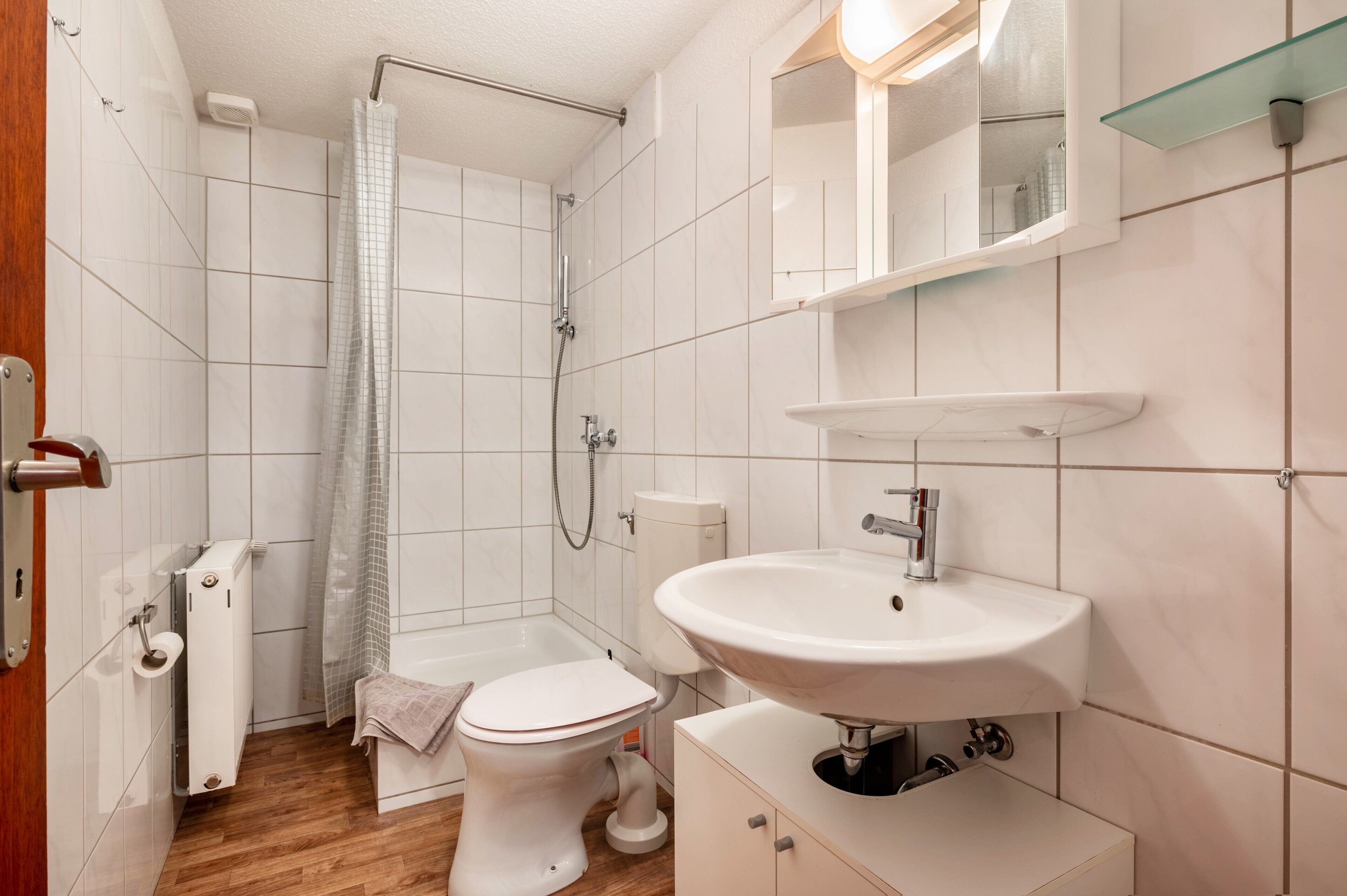 Ein Badezimmer mit Dusche, Toilette, Waschbecken und Ablagefläche aus Glas darüber.