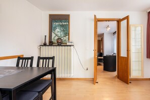 Un espace repas comprenant une table, des chaises, un radiateur, une œuvre d’art encadrée et une porte ouverte donnant sur une autre pièce.