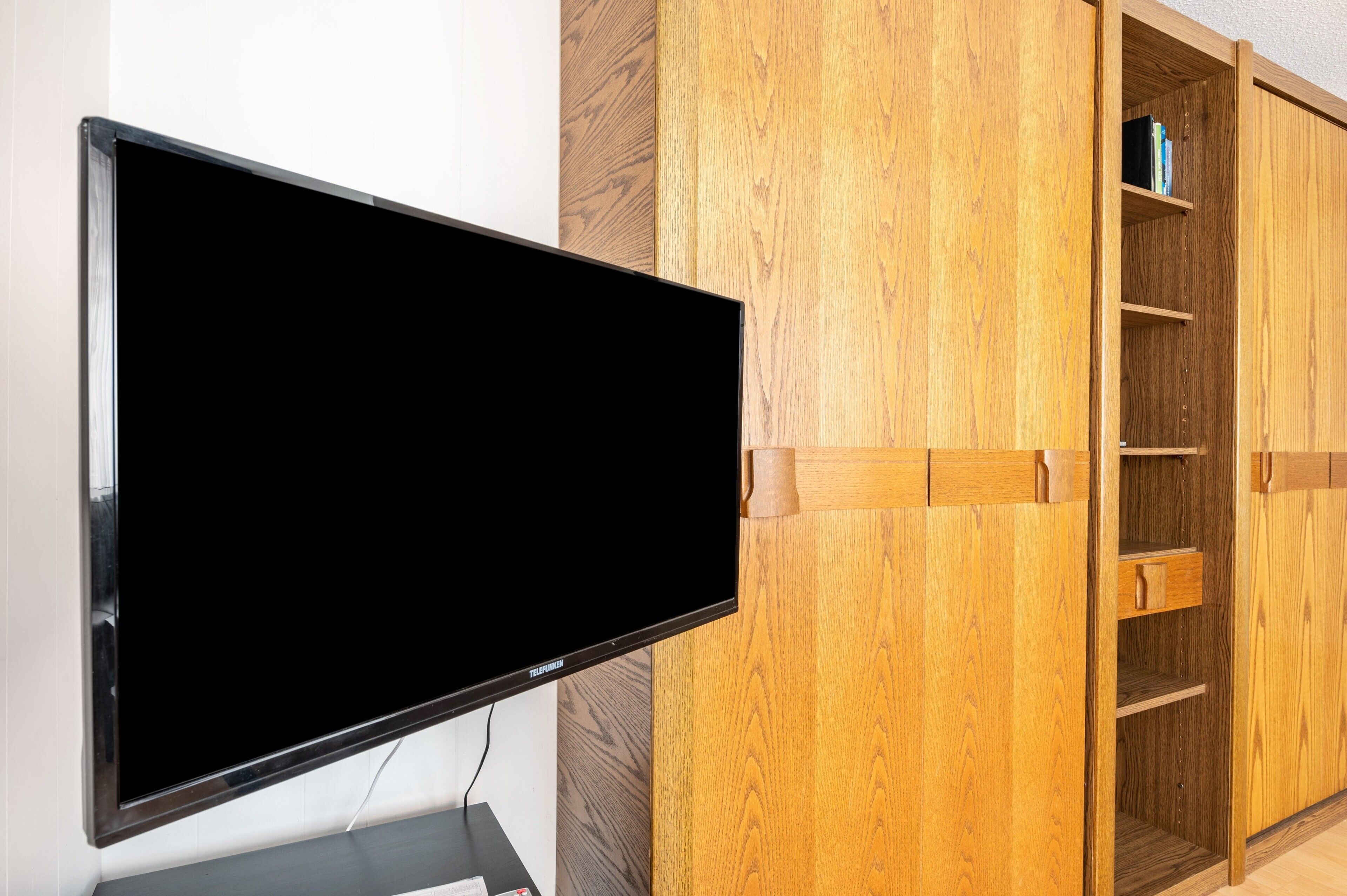 A flat-screen TV mounted on a wall, a wooden cabinet with shelves, and a drawer.