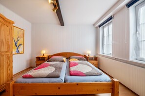Un lit double avec deux tables de chevet, une tête de lit en bois, un radiateur et une fenêtre avec des rideaux.