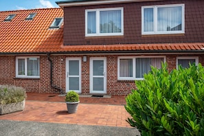 A two-story brick house with a red-tiled roof, white-framed windows, and a brick pathway leading to the entrance.