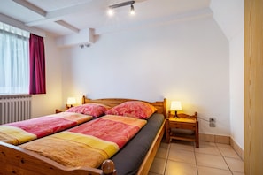 A double bed with a wooden frame, two bedside tables with lamps, a window with curtains, and a radiator.