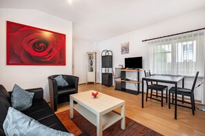 A modern living room with a black sofa, a coffee table, a dining table with chairs, a TV, and a large red rose painting on the wall. - Hus achtern Diek Cuxhaven Apartment No. 04 (Cuxhaven)