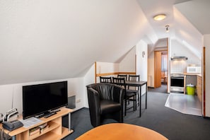 A compact living space with a television, seating, a kitchenette, and a dining area.