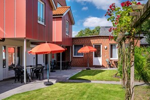 A patio with outdoor seating and umbrellas, a brick building, and a garden with flowers.