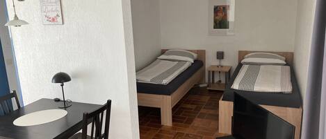 A compact room with a bed, a TV, a desk with a chair, and a small table.