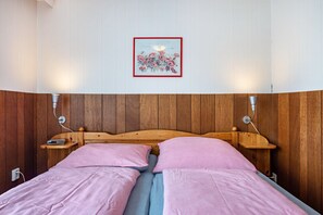 Un lit double avec une literie rose, une tête de lit en bois, des tables de chevet avec des lampes et un tableau encadré au mur.