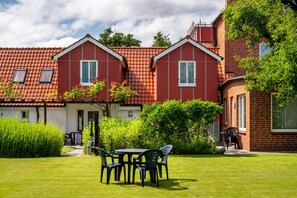 A two-story house with a red-tiled roof, a garden with a table and chairs, and a pathway leading to the entrance.
