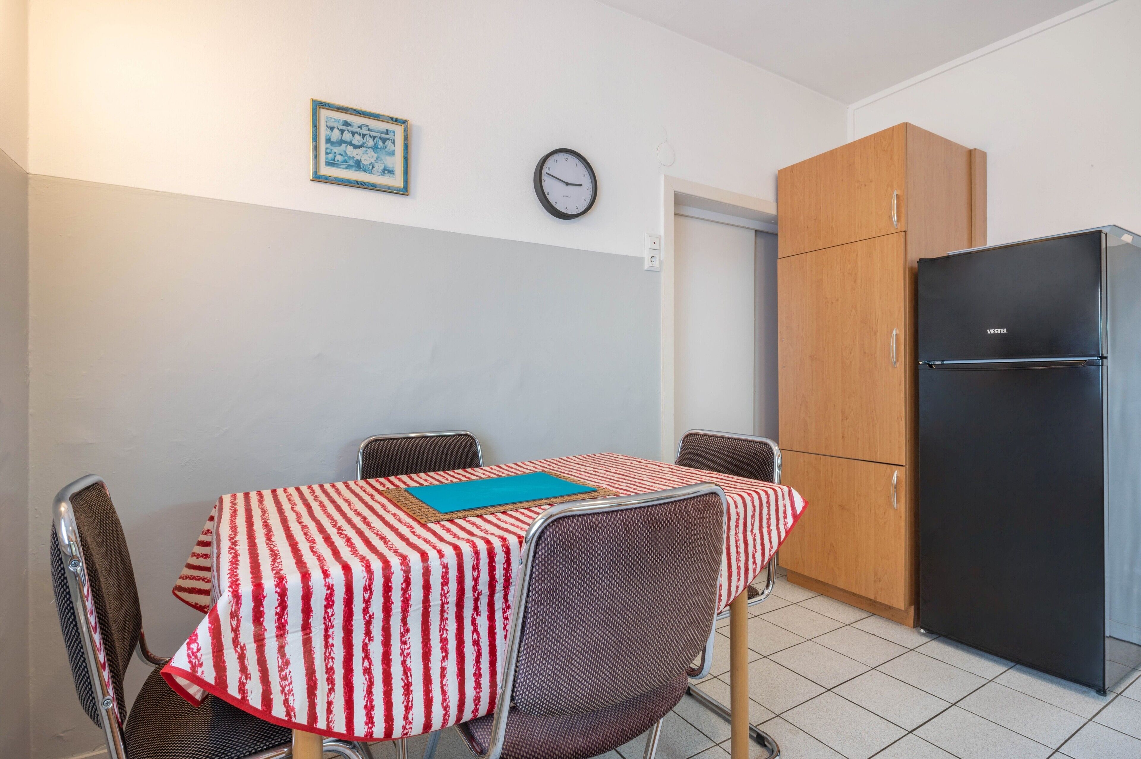 Une petite cuisine équipée d’une table à manger, de chaises, d’une horloge et d’un réfrigérateur.