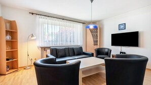 Uma sala de estar moderna com um sofá, duas poltronas, uma mesa de centro, uma televisão e uma estante de livros.