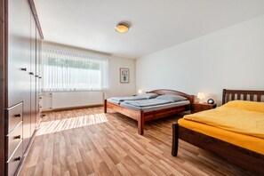 A bedroom with a wooden bed, a wooden wardrobe, a radiator, a window with blinds, and a framed picture on the wall.