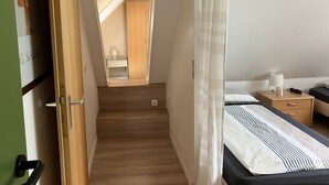 Ein Schlafzimmer mit einem Bett, einem Nachttisch, einem Spiegel und einer Tür zu einem anderen Raum.