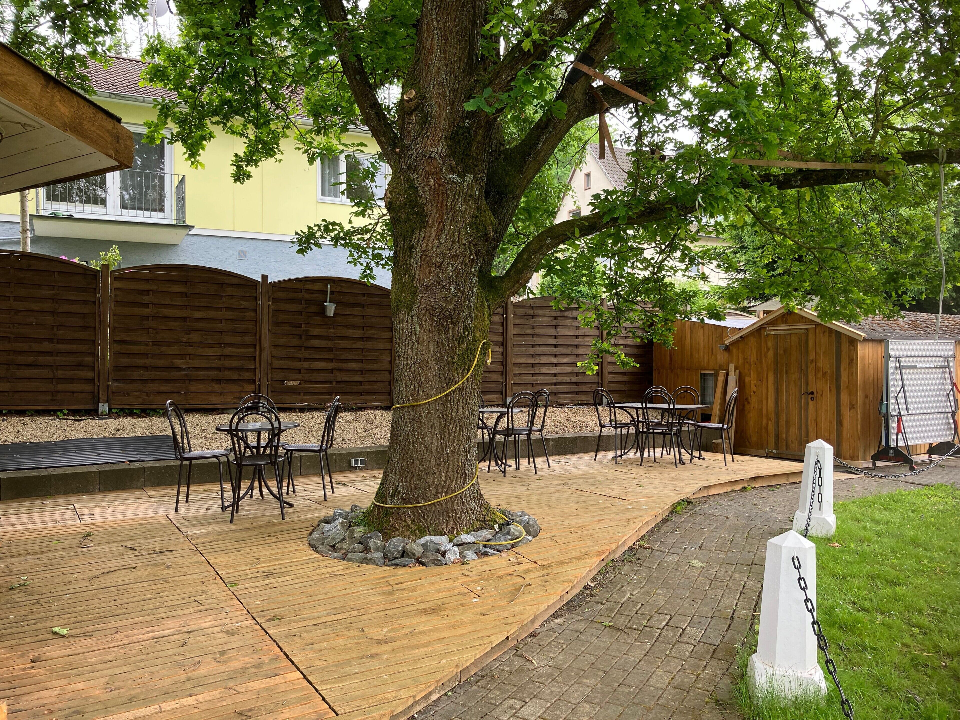 Een terras met bomen, buitenmeubels en een houten omheining.