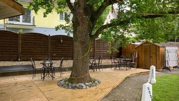 Een terras met bomen, buitenmeubels en een houten omheining.