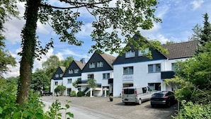 Eine Reihe weißer Gebäude mit dunklen Dächern, ein Parkplatz und ein Baum im Vordergrund.