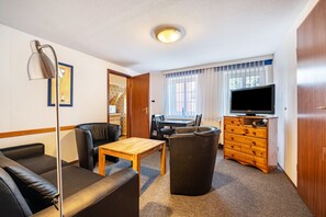 Ett rum med en soffa, ett bord, en tv, en byrå och ett fönster med gardiner.
