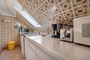 A kitchen with patterned wallpaper, a window, a sink, a toaster, and a trash bin.