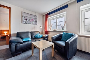 A modern living room with two leather sofas, a wooden coffee table, a painting on the wall, a window with curtains, and a radiator.