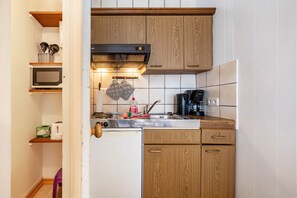 A compact kitchen with wooden cabinets, a microwave, a coffee maker, and a toaster.