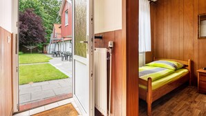 A room with a bed, a radiator, a small table, and a window with curtains. - Hus achtern Diek Cuxhaven Apartment No. 12 (Cuxhaven)