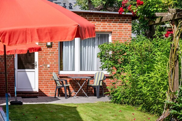 A brick house with a patio, a table, two chairs, and a red umbrella.