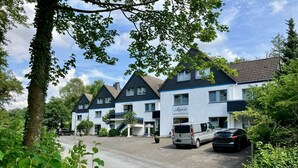 Een rij witte gebouwen met donkere daken, een parkeerplaats en een boom op de voorgrond.