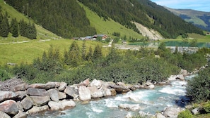 Un paysage montagneux avec une rivière, un chalet et un lac.