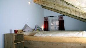 Une chambre avec un plafond en pente, un lit avec des oreillers, une table de chevet et une fenêtre avec des rideaux.