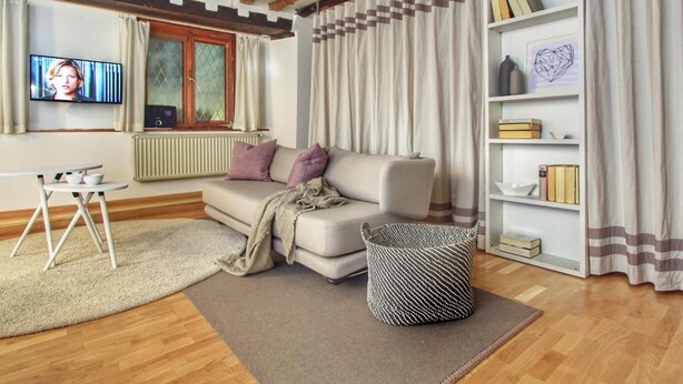 Ein Wohnzimmer mit einer Couch, einem Couchtisch, einem Fernseher, einem Bücherregal und einem Fenster mit Vorhängen.