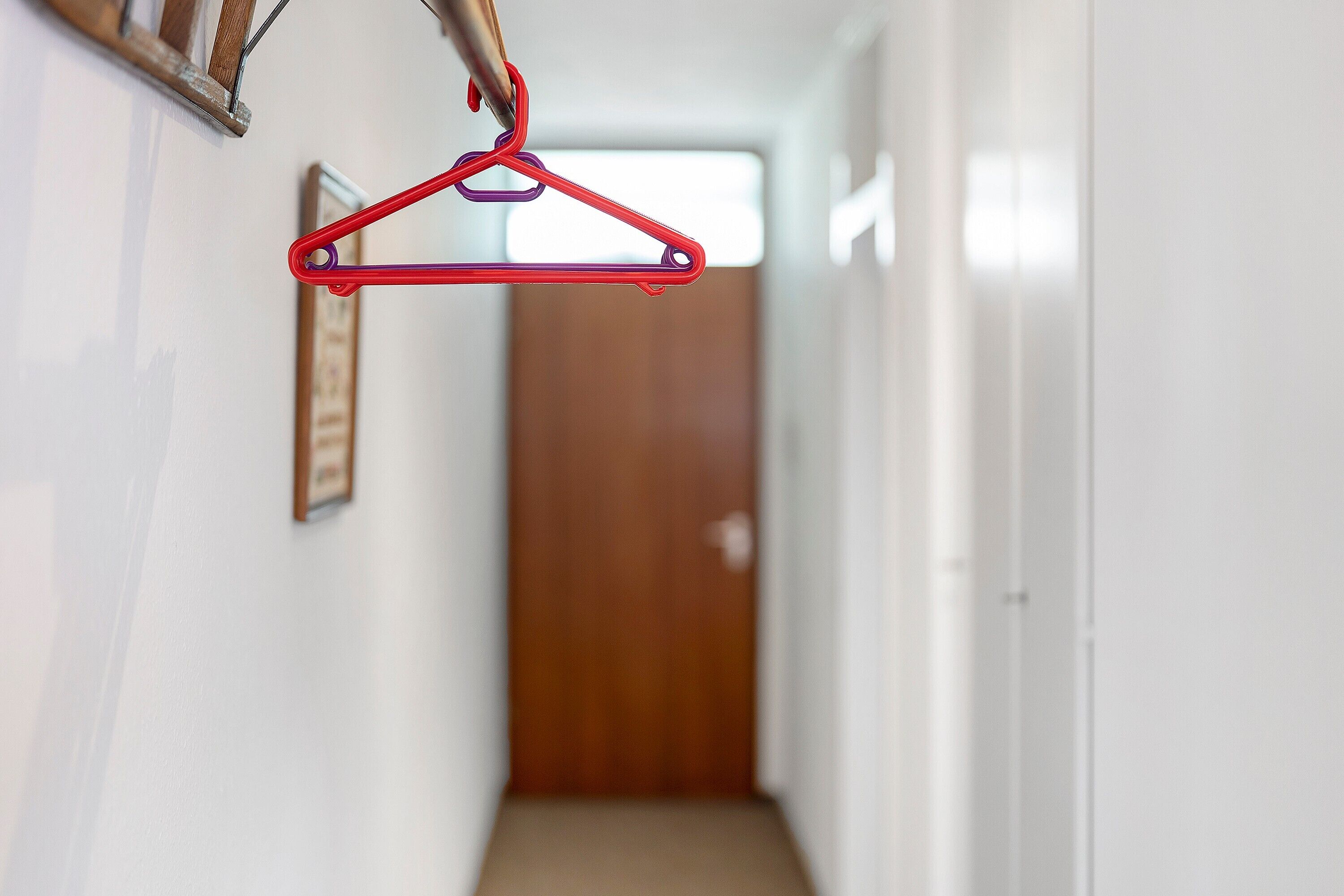 Un pasillo con un perchero rojo, una puerta de madera al final y un cuadro en la pared.