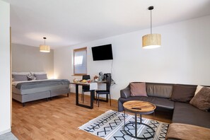 Ett modernt och väl upplyst rum med en säng, en soffa, en matplats och en tv som är monterad på väggen.
