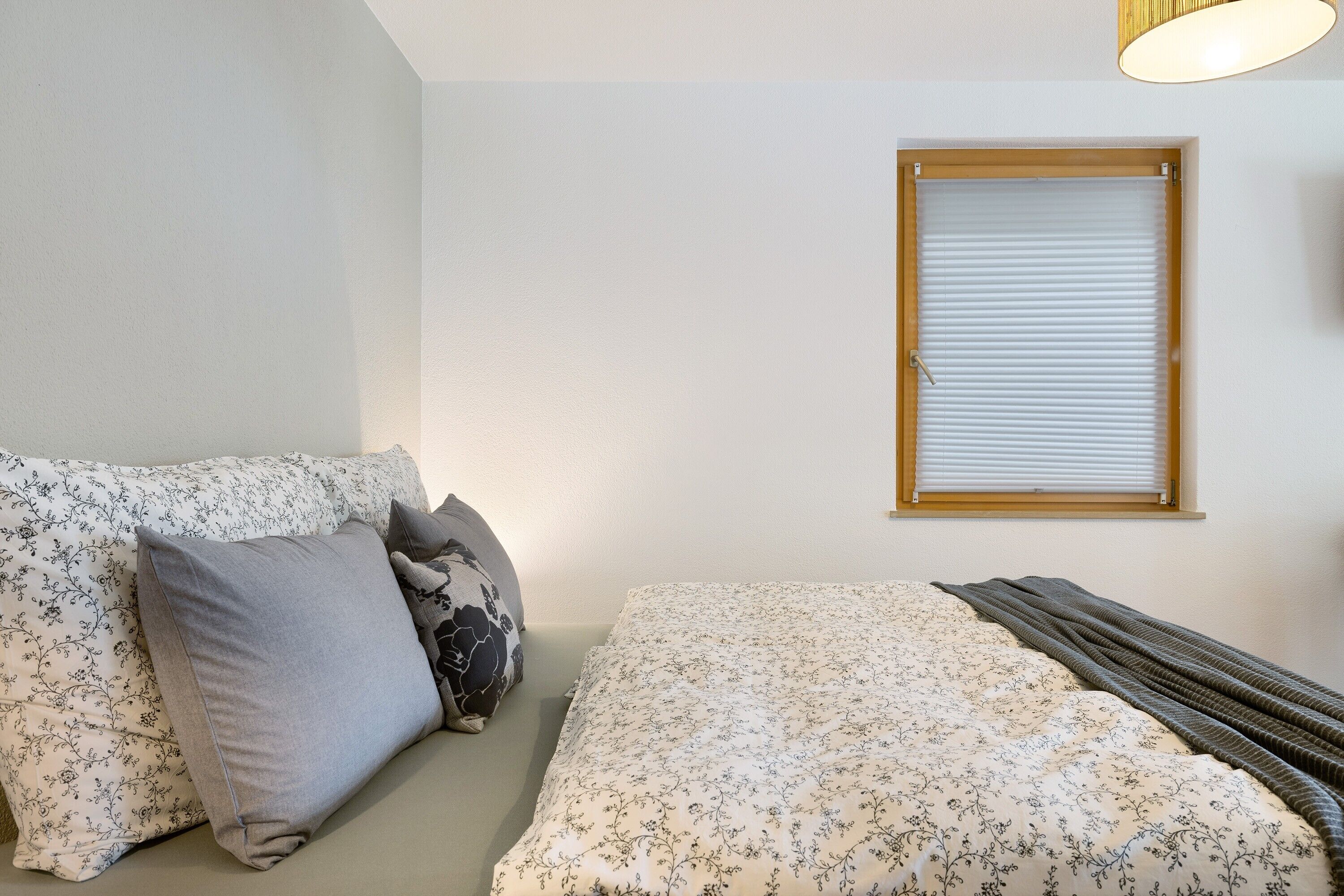 Ein Schlafzimmer mit einem Bett, einem Fenster mit Jalousien und einer Couch mit gemusterten Kissen.